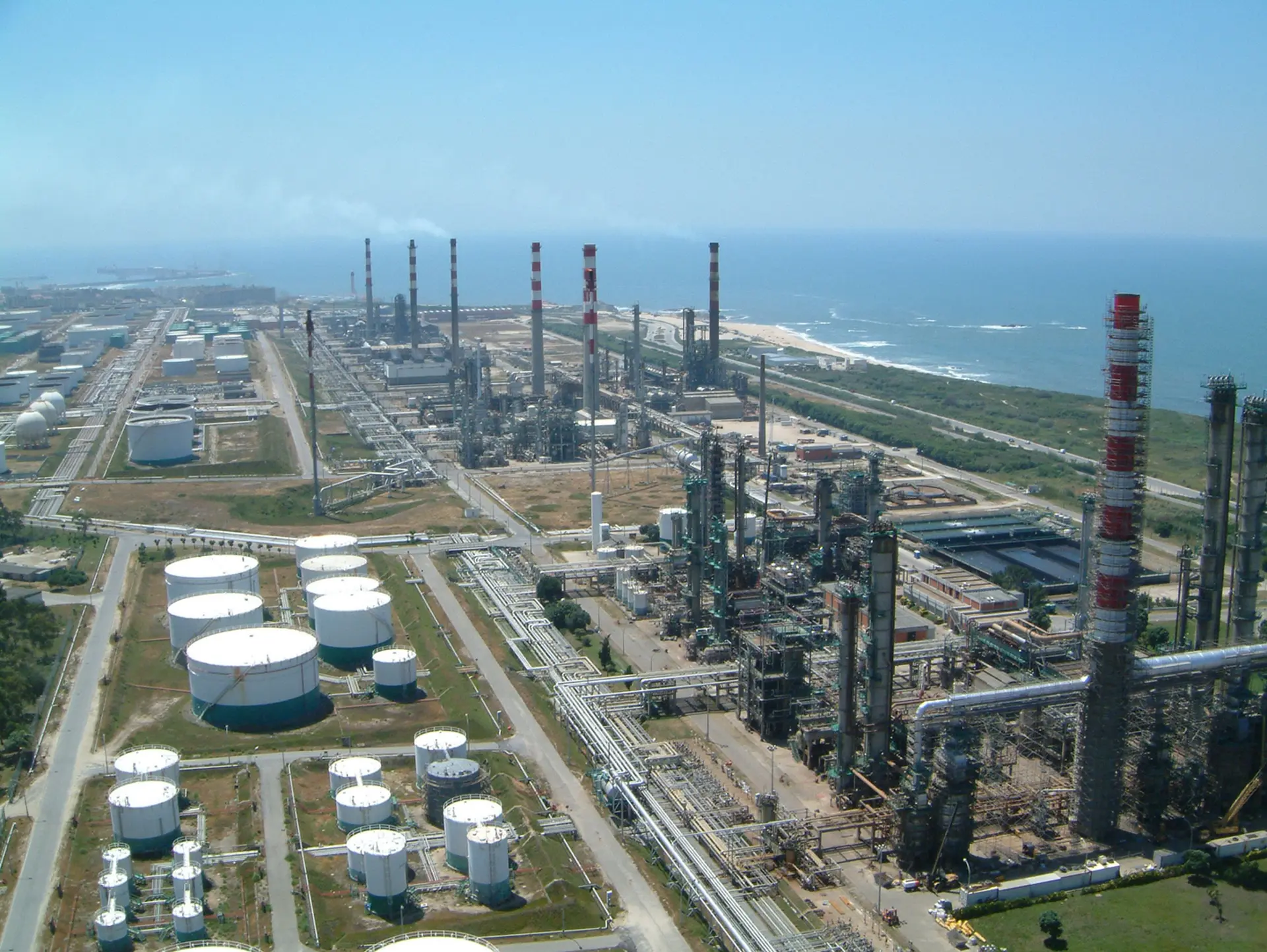 Aerial view of the Porto refinery conversion site with storage tanks, processing towers and coastal infrastructure